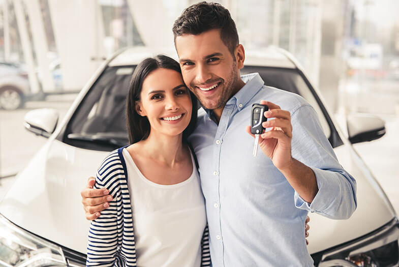 young couple holding up key to their new car